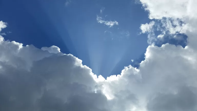 blue sky with sun rays coming out behind white clouds