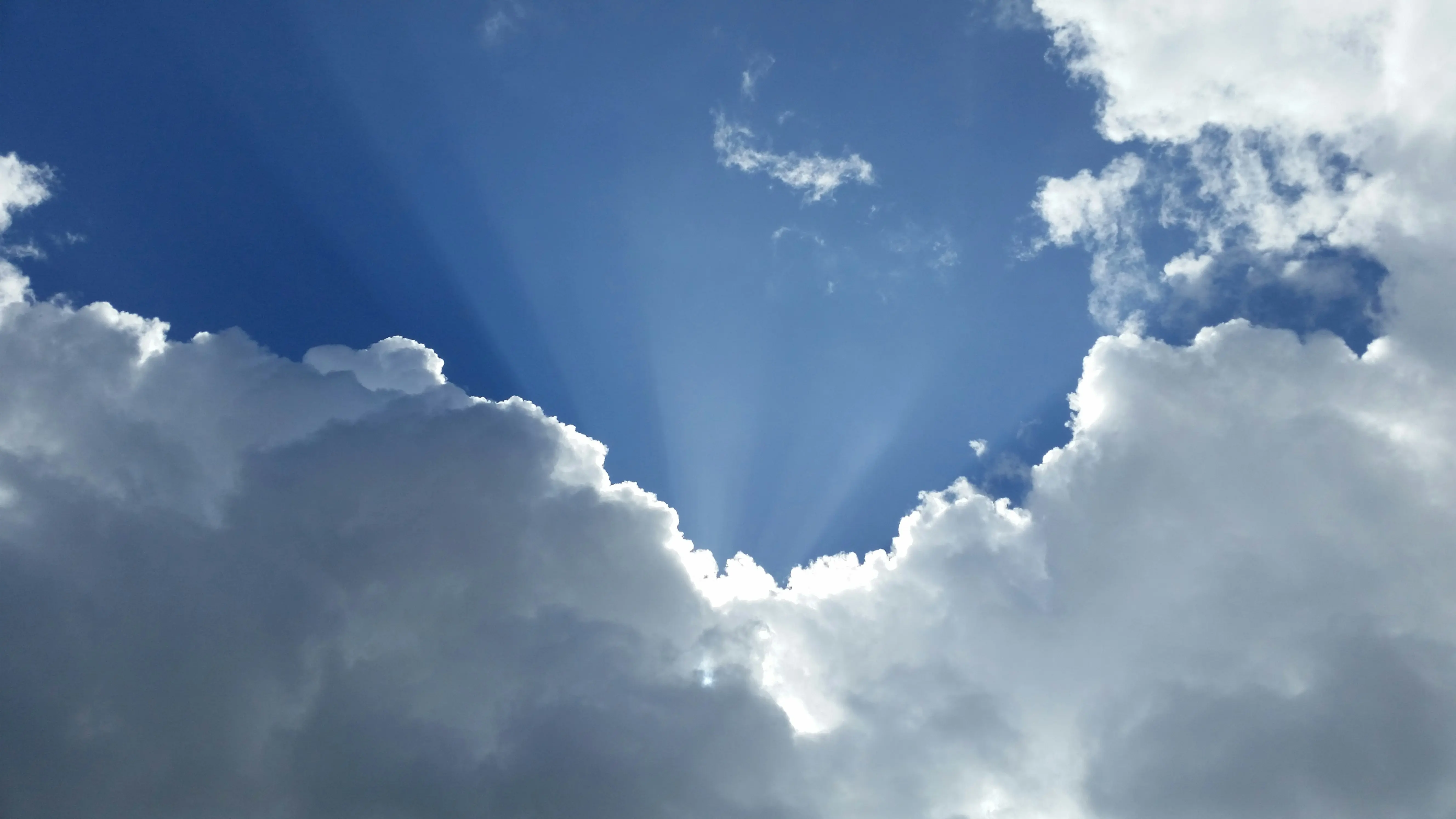 blue sky with sun rays coming out behind white clouds